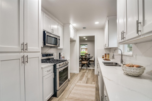 1106 Spring Lake Dr, Garland, TX 75043 - kitchen featuring stainless steel appliances, a sink, white cabinets, light wood finished floors, and light stone counters