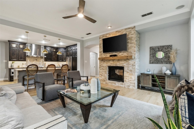 5213 Evening Sun Dr, Frisco, TX 75034 - living area featuring light wood finished floors, ceiling fan, arched walkways, crown molding, and a stone fireplace