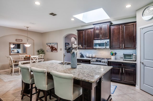 3103 Whispering Pine Blvd, Melissa, TX 75454 - kitchen featuring stainless steel appliances, arched walkways, light tile patterned floors, light stone counters, and hanging light fixtures