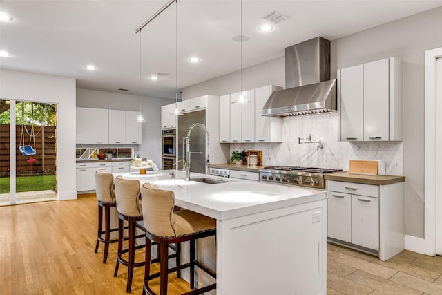 5624 Melshire Dr, Dallas, TX 75230 - kitchen with wall chimney exhaust hood, a sink, tasteful backsplash, a breakfast bar, and an island with sink