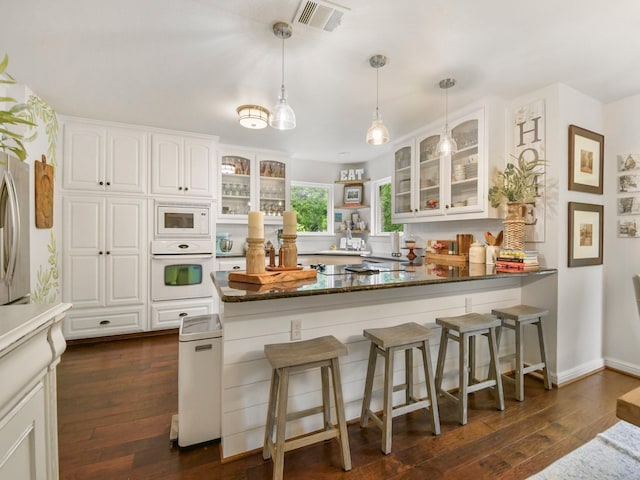 1951 Ravenwood Dr, Keller, TX 76262 - kitchen with white appliances, a peninsula, white cabinetry, a breakfast bar area, and dark wood finished floors