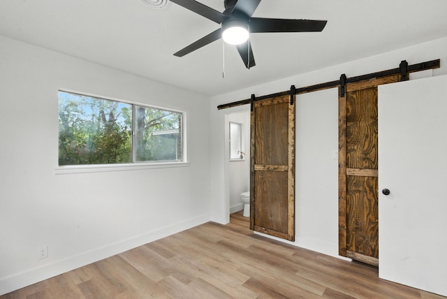 1423 W Ball St, Weatherford, TX 76086 - unfurnished bedroom featuring a barn door, light wood finished floors, connected bathroom, and ceiling fan