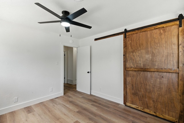 1423 W Ball St, Weatherford, TX 76086 - unfurnished bedroom featuring a barn door, wood finished floors, and ceiling fan