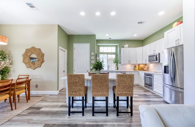 10108 Hunter Run, Frisco, TX 75035 - kitchen with appliances with stainless steel finishes, white cabinetry, a breakfast bar area, light wood-style floors, and recessed lighting