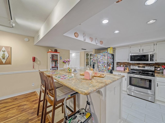 1824 Castille Dr, Carrollton, TX 75007 - kitchen featuring stainless steel appliances, white cabinets, a breakfast bar area, light stone countertops, and recessed lighting