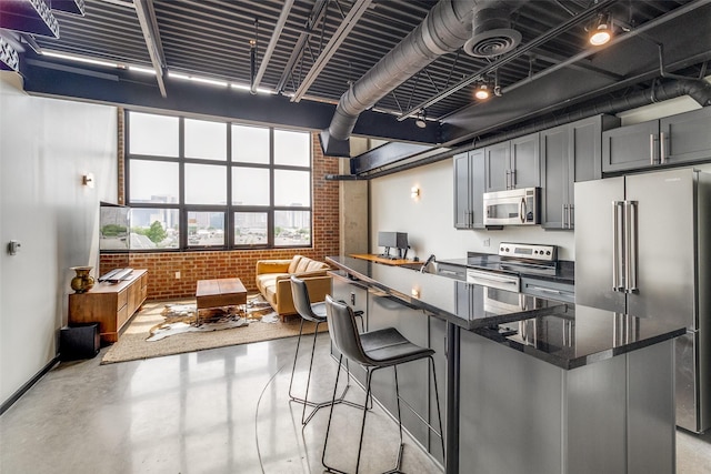 3110 Thomas Ave Unit 535, Dallas, TX 75204 - kitchen with stainless steel appliances, brick wall, finished concrete floors, a kitchen breakfast bar, and dark stone counters