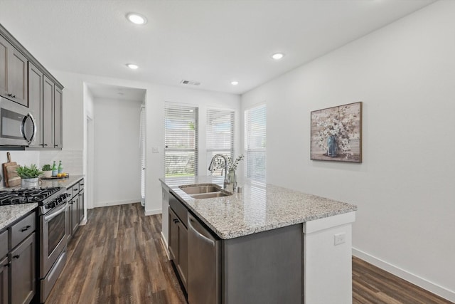 1012 Friesian Ln, Aubrey, TX 76227 - kitchen with appliances with stainless steel finishes, a sink, dark wood-type flooring, an island with sink, and light stone counters