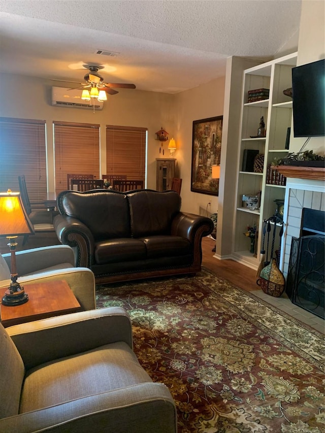 151 Summer Place Cir, Pottsboro, TX 75076 - living room featuring ceiling fan, a tiled fireplace, a textured ceiling, a wall unit AC, and wood finished floors