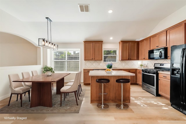 479 Sausalito Dr, Rockwall, TX 75087 - kitchen with black appliances, a center island, backsplash, light wood-type flooring, and light countertops
