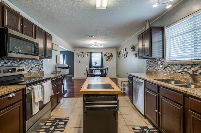 7419 Concordia Ln, Dallas, TX 75241 - kitchen with appliances with stainless steel finishes, a sink, a textured ceiling, backsplash, and dark brown cabinetry