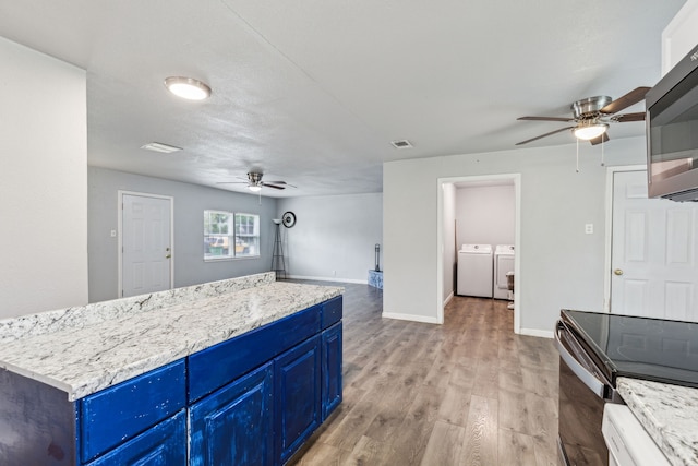 5225 Ira St N, Haltom City, TX 76117 - kitchen with a ceiling fan, blue cabinetry, separate washer and dryer, stainless steel microwave, and light wood-type flooring