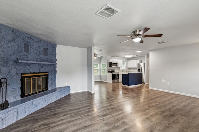 5225 Ira St N, Haltom City, TX 76117 - unfurnished living room featuring ceiling fan, dark wood-style floors, a stone fireplace, baseboards, and a sink