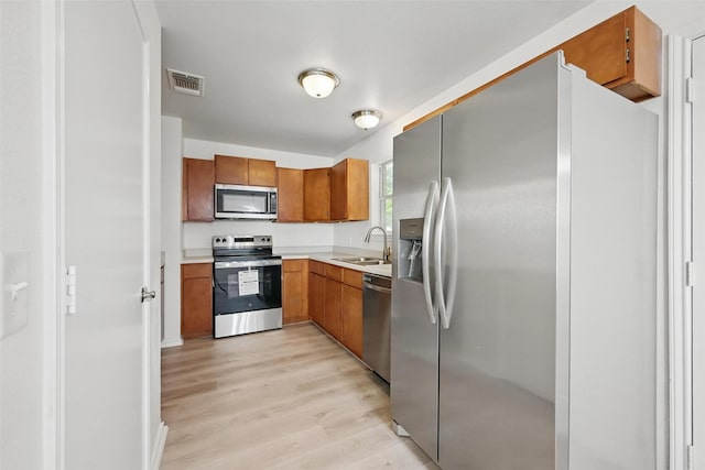 714 E 12th St, Bonham, TX 75418 - kitchen featuring appliances with stainless steel finishes, a sink, light wood-type flooring, and brown cabinets