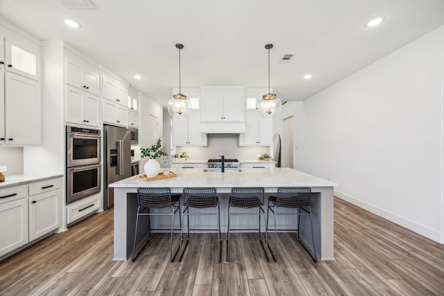 927 Leola Ln, Allen, TX 75013 - kitchen featuring stainless steel appliances, wood finished floors, white cabinetry, a breakfast bar, and a center island with sink