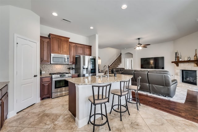 1003 Stanbridge Dr, Wylie, TX 75098 - kitchen featuring appliances with stainless steel finishes, a breakfast bar, a fireplace, light stone countertops, and a center island with sink