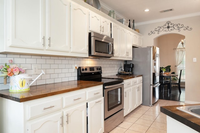 14221 Tijuana Trl, Fort Worth, TX 76052 - kitchen with appliances with stainless steel finishes, light tile patterned floors, ornamental molding, white cabinetry, and decorative backsplash