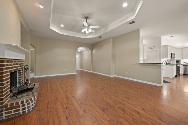 6345 Pinionpark Way, Fort Worth, TX 76179 - unfurnished living room featuring a raised ceiling, a ceiling fan, a brick fireplace, arched walkways, and recessed lighting