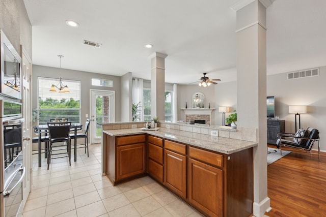 11487 Balcones Dr, Frisco, TX 75033 - kitchen featuring a fireplace, ornate columns, open floor plan, a ceiling fan, and brown cabinets