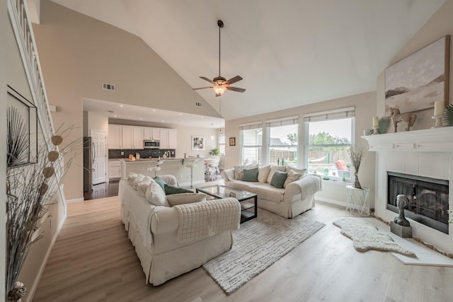 5309 Chatsworth Ln, Fort Worth, TX 76244 - living room with light wood-type flooring, ceiling fan, high vaulted ceiling, a tiled fireplace, and baseboards