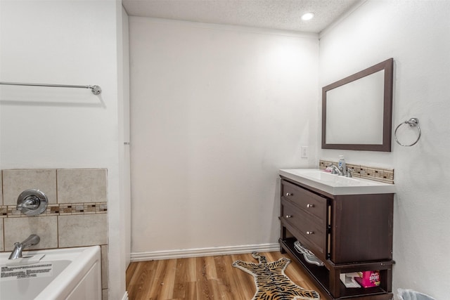 216 E Tennie St, Gainesville, TX 76240 - bathroom with vanity, a bath, a textured ceiling, wood finished floors, and baseboards