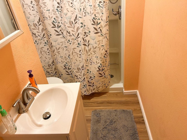1611 Ave B, Dallas, TX 75203 - bathroom featuring wood finished floors, a shower stall, a textured wall, baseboards, and vanity