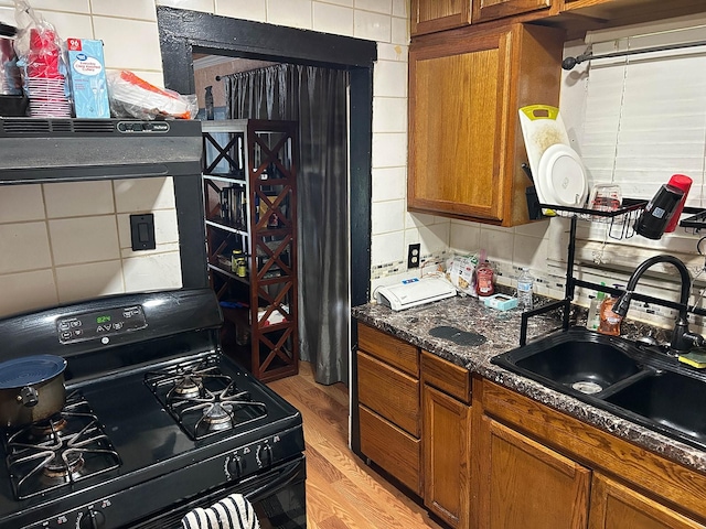 1611 Ave B, Dallas, TX 75203 - kitchen featuring black gas range, brown cabinetry, a sink, tasteful backsplash, and light wood-style floors