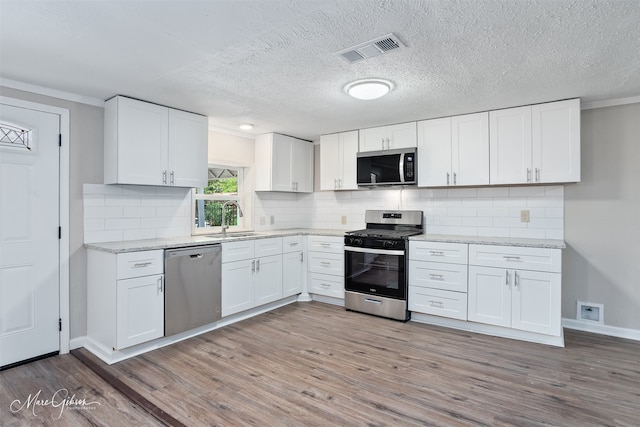 4210 Via St, Shreveport, LA 71109 - kitchen featuring appliances with stainless steel finishes, a sink, wood finished floors, white cabinetry, and ornamental molding