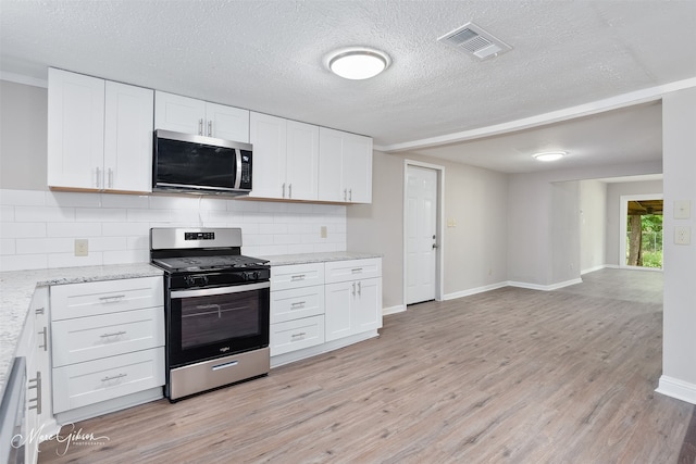 4210 Via St, Shreveport, LA 71109 - kitchen featuring appliances with stainless steel finishes, light wood finished floors, backsplash, white cabinets, and a textured ceiling