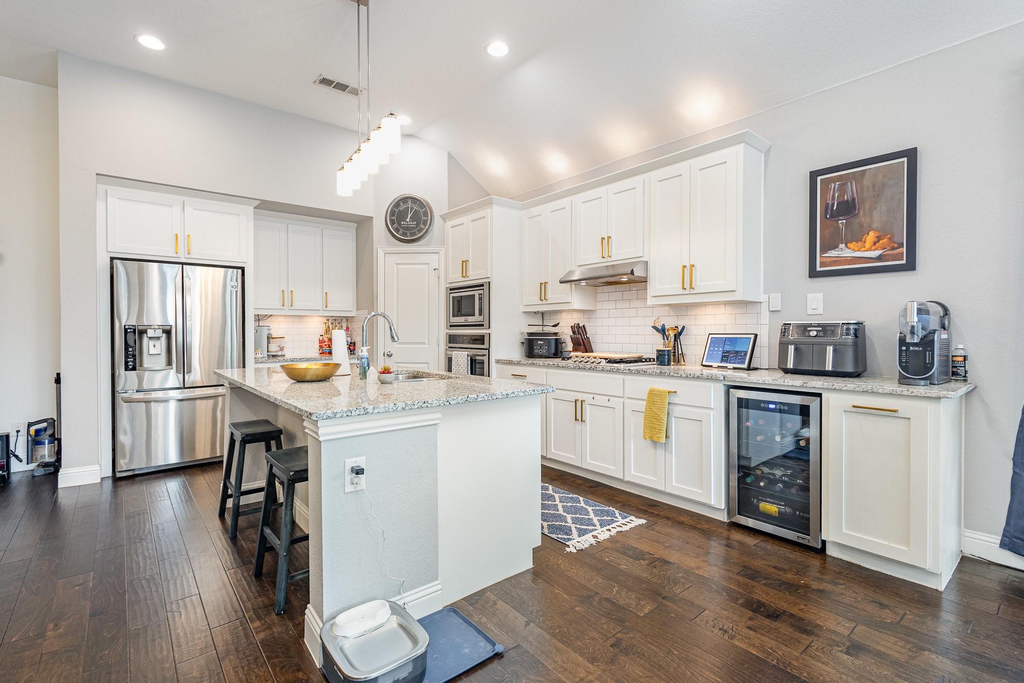 1502 Barley Ct, Forney, TX 75126 - kitchen with appliances with stainless steel finishes, beverage cooler, a sink, under cabinet range hood, and a breakfast bar area