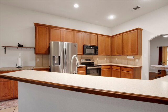 1212 Live Oak St, Royse City, TX 75189 - kitchen featuring appliances with stainless steel finishes, arched walkways, decorative backsplash, light countertops, and brown cabinetry