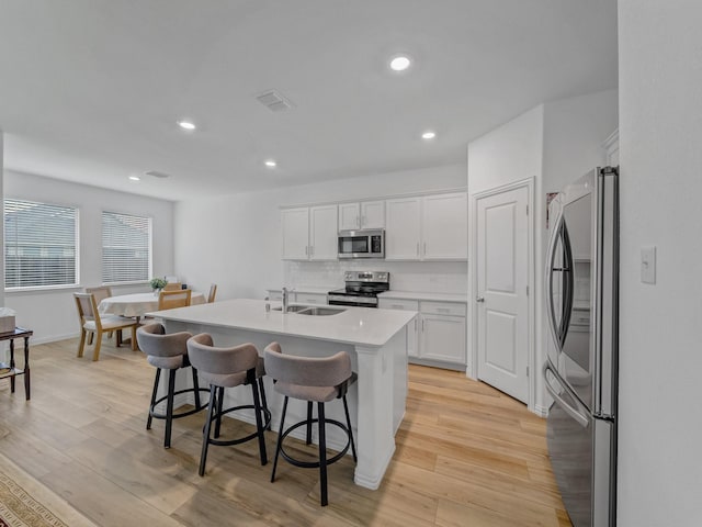 316 Crossvine Way, Princeton, TX 75407 - kitchen with stainless steel appliances, a sink, white cabinetry, light wood finished floors, and a breakfast bar
