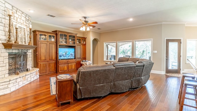 1851 Rock Church Hwy, Tolar, TX 76476 - living area with arched walkways, a stone fireplace, dark wood finished floors, ceiling fan, and crown molding