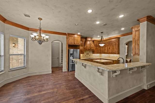 608 Guadalupe Rd, Keller, TX 76248 - kitchen featuring arched walkways, stainless steel fridge with ice dispenser, light stone counters, dark wood-style floors, and brown cabinetry