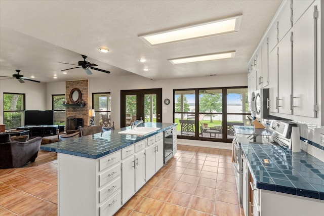 7016 Fm 3054, Malakoff, TX 75148 - kitchen with stainless steel appliances, tile counters, a sink, a brick fireplace, and white cabinets