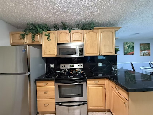 112 Plainview Dr, Wylie, TX 75098 - kitchen with appliances with stainless steel finishes, light brown cabinetry, a textured ceiling, a peninsula, and backsplash