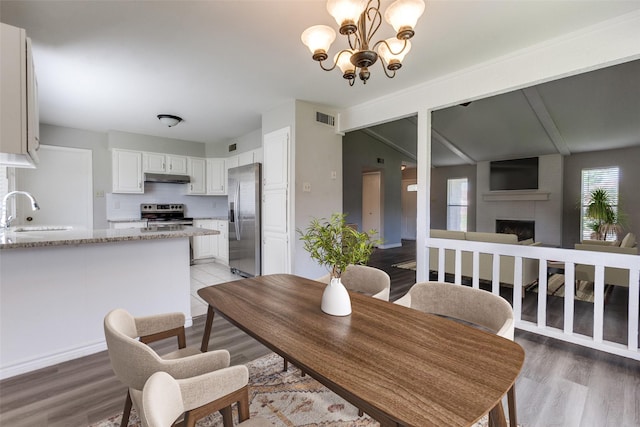 2513 Figtree Ln, Plano, TX 75074 - dining area with a fireplace, light wood finished floors, a chandelier, and baseboards