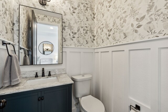 5221 Sylvan Shores Dr, Frisco, TX 75036 - half bath featuring wallpapered walls, vanity, a wainscoted wall, toilet, and a decorative wall