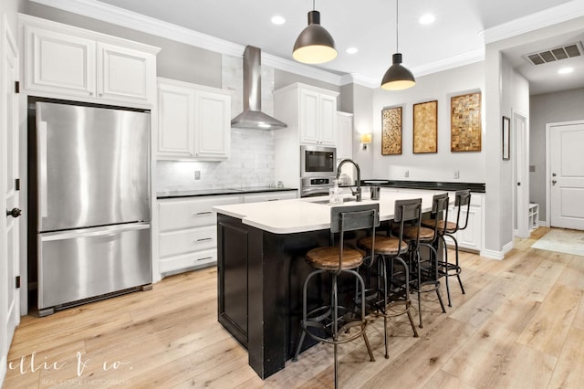 2409 Lynbrook Dr, Abilene, TX 79606 - kitchen featuring appliances with stainless steel finishes, wall chimney range hood, an island with sink, tasteful backsplash, and white cabinetry