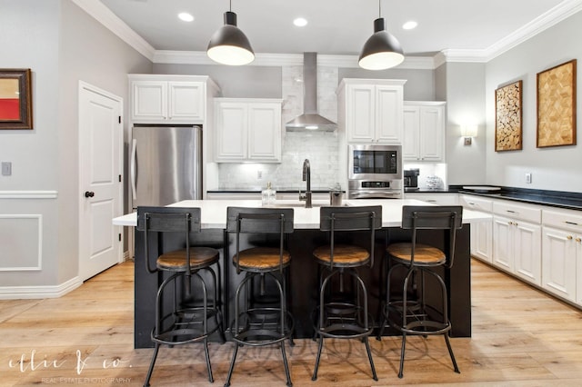 2409 Lynbrook Dr, Abilene, TX 79606 - kitchen with wall chimney exhaust hood, stainless steel appliances, ornamental molding, a kitchen island with sink, and light wood-style flooring