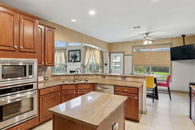 269 Love Bird Ln, Murphy, TX 75094 - kitchen featuring stainless steel appliances, a sink, a peninsula, light stone countertops, and brown cabinetry