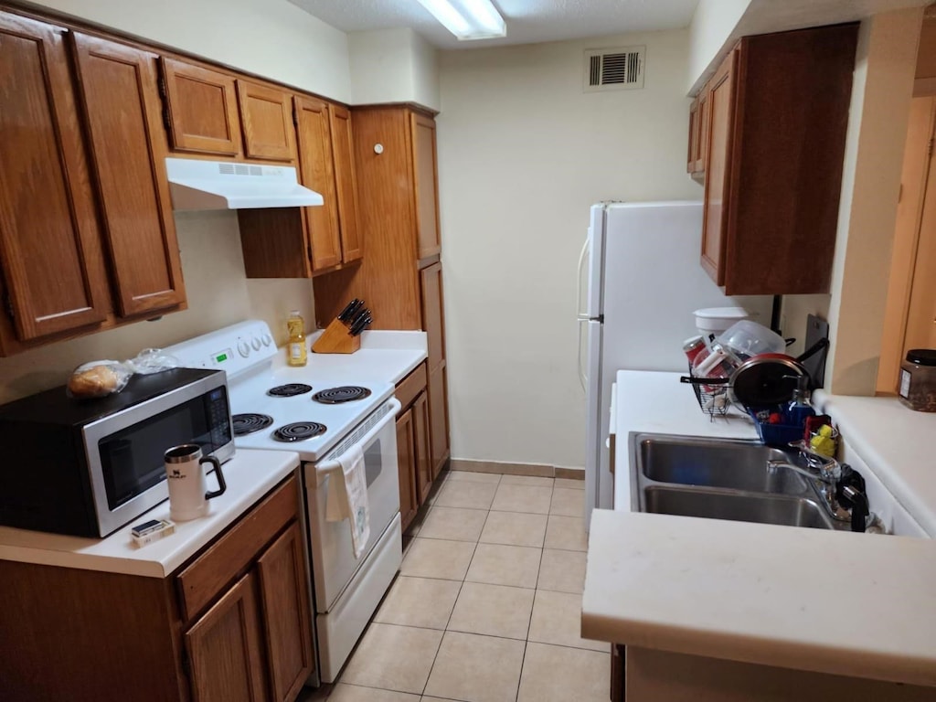 3624 Parkridge Dr Unit 213, Dallas, TX 75234 - kitchen with stainless steel microwave, white electric range oven, under cabinet range hood, brown cabinetry, and light countertops