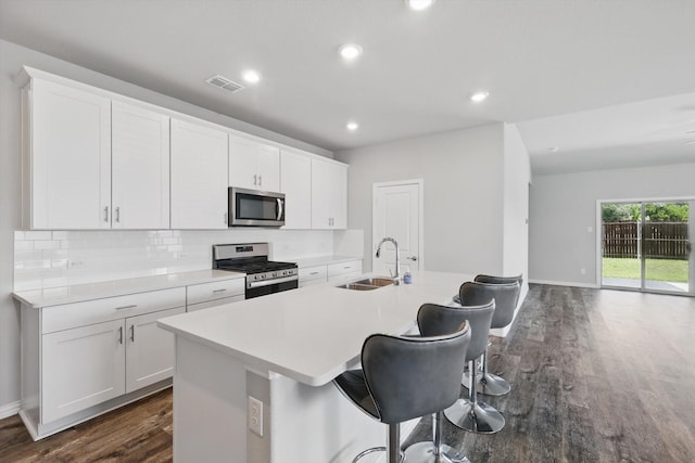 6112 Fire Water Dr, Fort Worth, TX 76179 - kitchen with appliances with stainless steel finishes, a sink, dark wood-type flooring, a center island with sink, and decorative backsplash