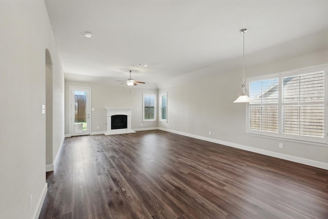 7802 Lindsey Dr, Rowlett, TX 75088 - unfurnished living room with a ceiling fan, dark wood-style floors, baseboards, arched walkways, and a fireplace with raised hearth