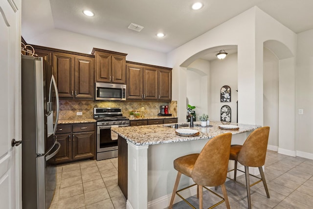 403 Woodbine Dr, Sherman, TX 75092 - kitchen featuring stainless steel appliances, decorative backsplash, light stone counters, arched walkways, and a kitchen bar