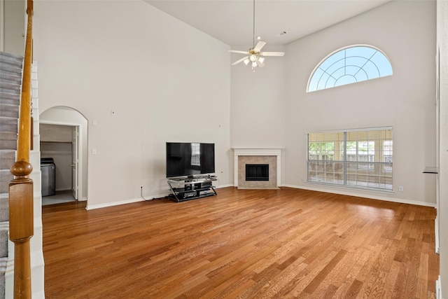 1117 Ruby St, Plano, TX 75094 - unfurnished living room with a high ceiling, a tiled fireplace, light wood-style flooring, a ceiling fan, and plenty of natural light