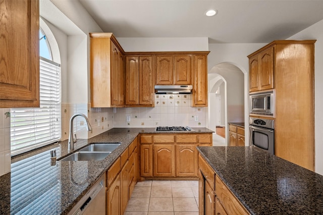 1117 Ruby St, Plano, TX 75094 - kitchen with stainless steel appliances, a sink, under cabinet range hood, dark stone countertops, and arched walkways