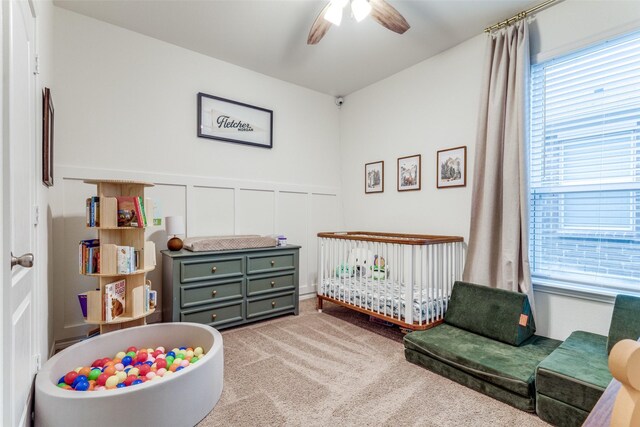 8744 Sleepy Daisy Dr, Fort Worth, TX 76131 - carpeted bedroom with multiple windows, a crib, a wainscoted wall, a decorative wall, and a ceiling fan