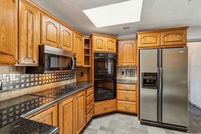 3109 Bullock Dr, Plano, TX 75023 - kitchen with black appliances, decorative backsplash, brown cabinetry, dark stone counters, and a skylight