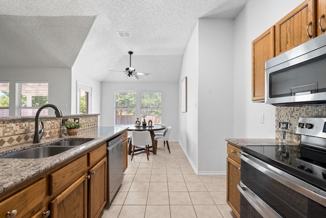 1132 Singletree Dr, Forney, TX 75126 - kitchen with stainless steel appliances, a sink, decorative backsplash, brown cabinetry, and a textured ceiling