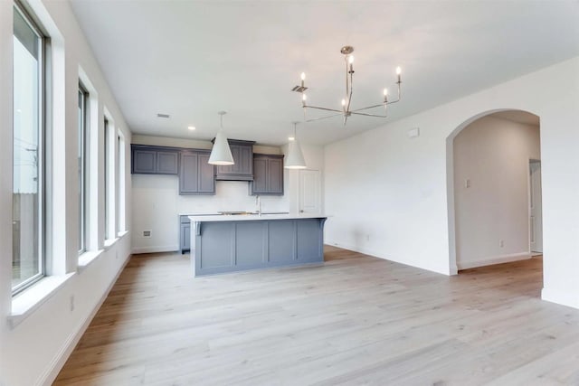 2316 Glasgow Way, Denton, TX 76207 - kitchen with light wood-style floors, an island with sink, a chandelier, arched walkways, and light countertops